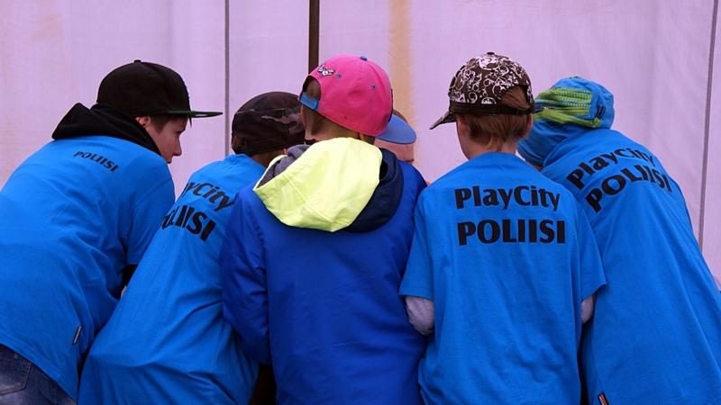 Playcityn poliisit kokoontuneena juttelemaan keskenään sinisissä Playcityn poliisi-t-paidoissa.