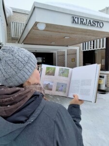 Luonto lainassa viikolla kirjastossa esillä aiheeseen liittyviä kirjoja. Kuvassa nainen lukemassa lintukirjaa ulkona kirjaston edessä.